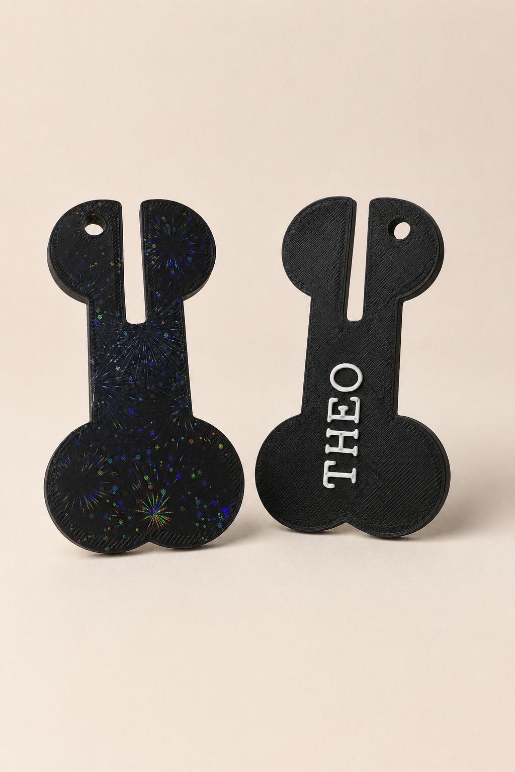 Black bone-shaped personalized pet waste bag carriers, one with a fireworks finish and one personalized with the name THEO